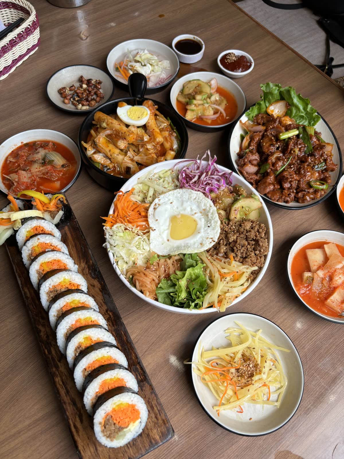 A table filled with vibrant Korean dishes, including kimbap rolls, bibimbap with a fried egg, tteokbokki, kimchi stew, and various side dishes. — How much sodium is in kimchi?