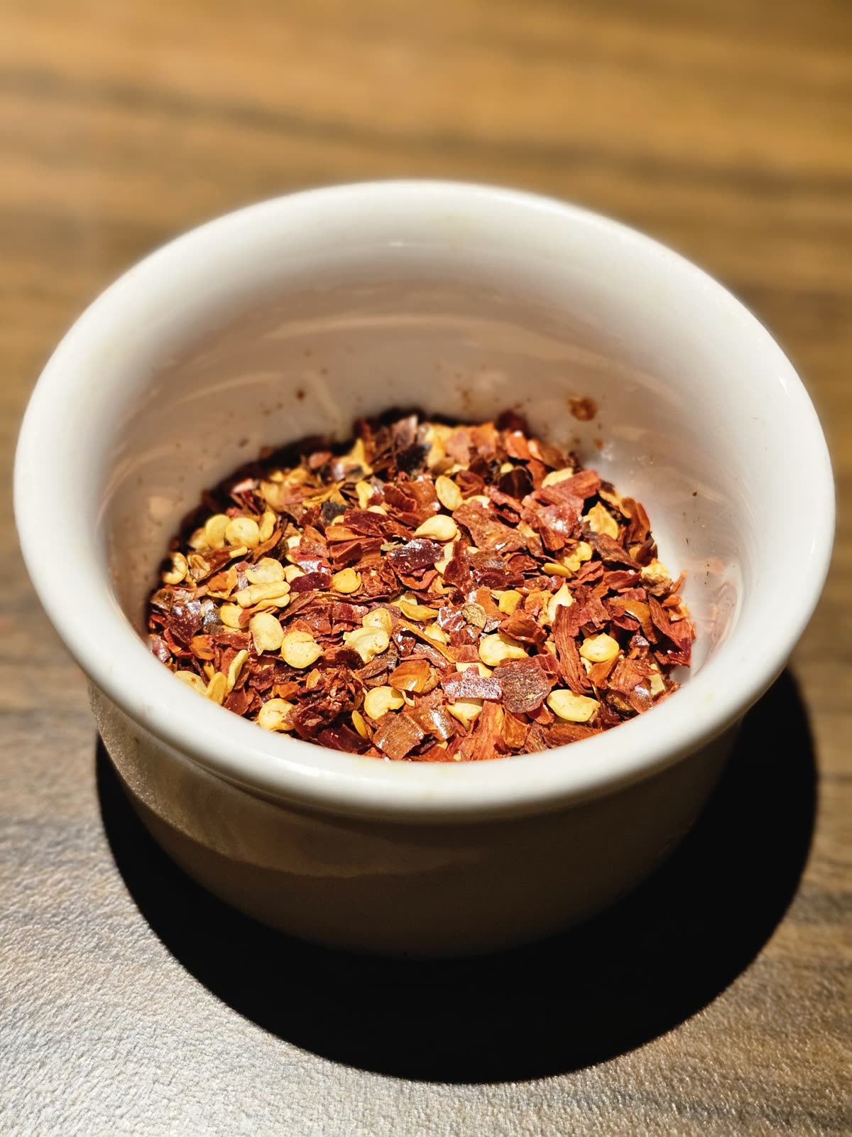 Close-up of red chili flakes in a white ceramic bowl on a wooden table, captured under warm light at a restaurant in Kozhikode. — Korean Spice Levels 0-3 Mapped to Indian Regional Heat