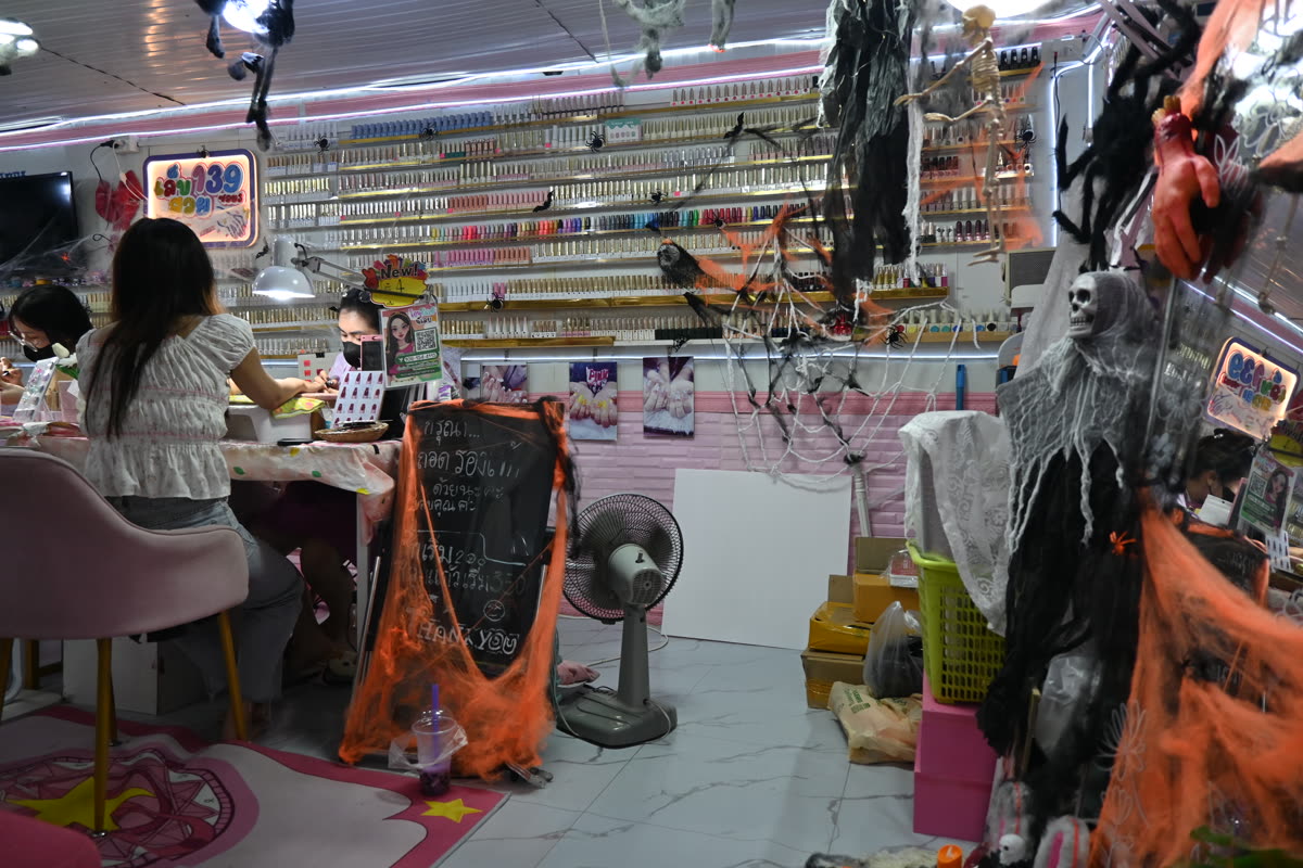 DFC 2093 A brightly lit nail salon decked out with Halloween decorations - cobwebs skulls and orange streamers - while customers sit at a manicure station with rows of nail polish bottles on the wall behind — Korean Nail Salon Seoul: How Booking Works Without a Korean Phone