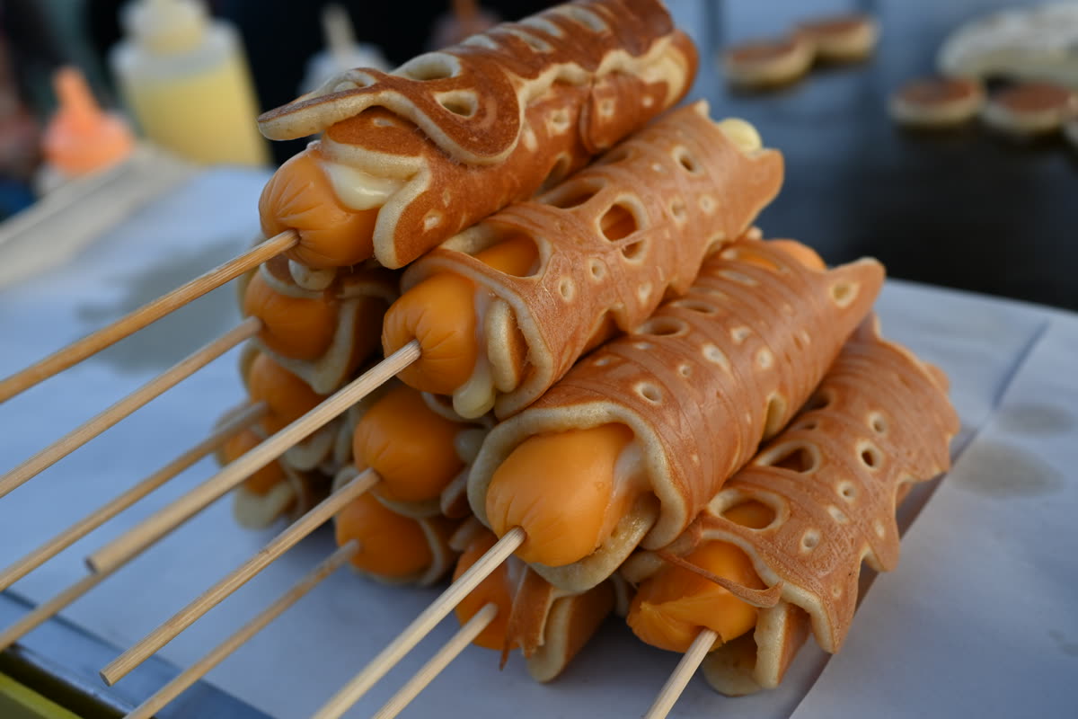DFC 3932 Golden cheesy corn dogs hot dogs on sticks wrapped in crispy hole-punched pancake batter stacked and ready to enjoy — Korean Corn Dog Recipe at Home: The Short Answer